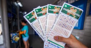 Mão segurando talões da Mega-Sena dentro de casa lotérica
