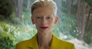 Tilda Swinton olhando para a cãmera, de roupa amarela