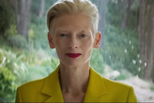 Tilda Swinton olhando para a cãmera, de roupa amarela