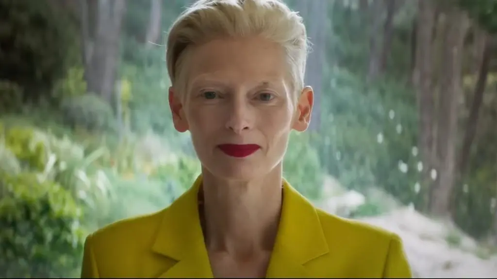 Tilda Swinton olhando para a cãmera, de roupa amarela