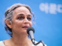 Arundhati Roy Berlinale de cabelo preso, falando em microfone, sem olhar para a câmera