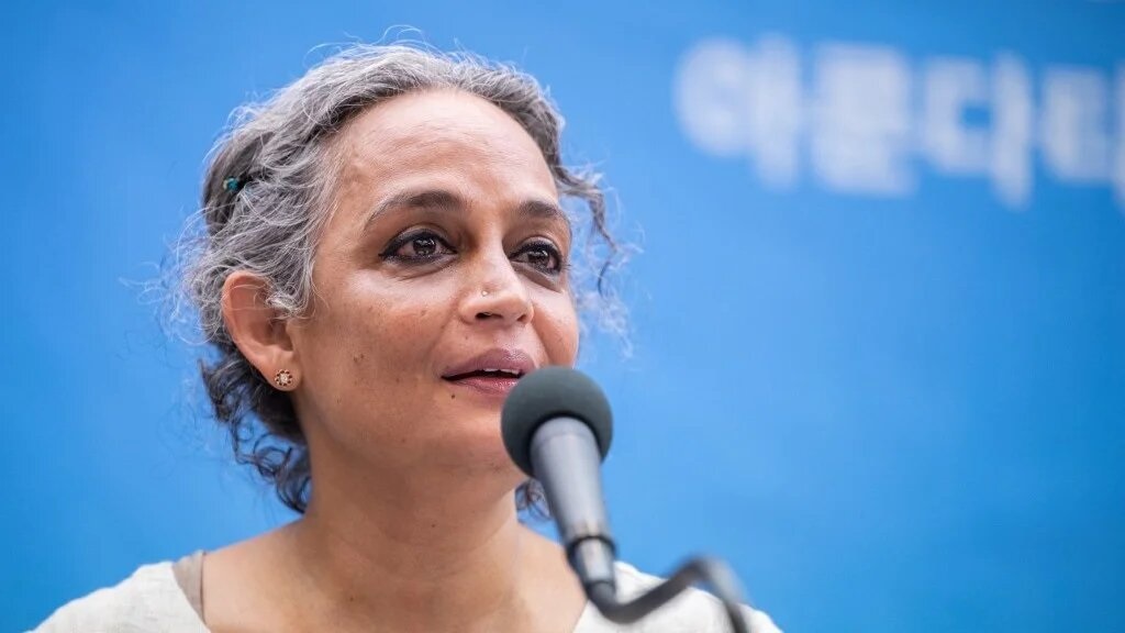 Arundhati Roy Berlinale de cabelo preso, falando em microfone, sem olhar para a câmera