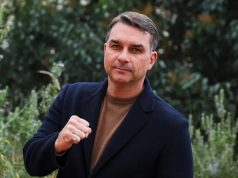 o senador Flávio Bolsonaro de roupa preta e marrom, posando para foto com as mãos fechadas