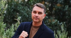 o senador Flávio Bolsonaro de roupa preta e marrom, posando para foto com as mãos fechadas