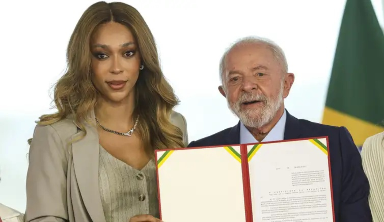 deputada federal Érika Hilton (PSOL) e Lula posando para foto lado a lado, ambos sérios, segurando papel