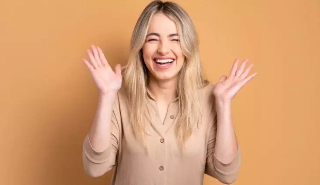 Mulher loira de camisa social bege e cabelo solto, rindo