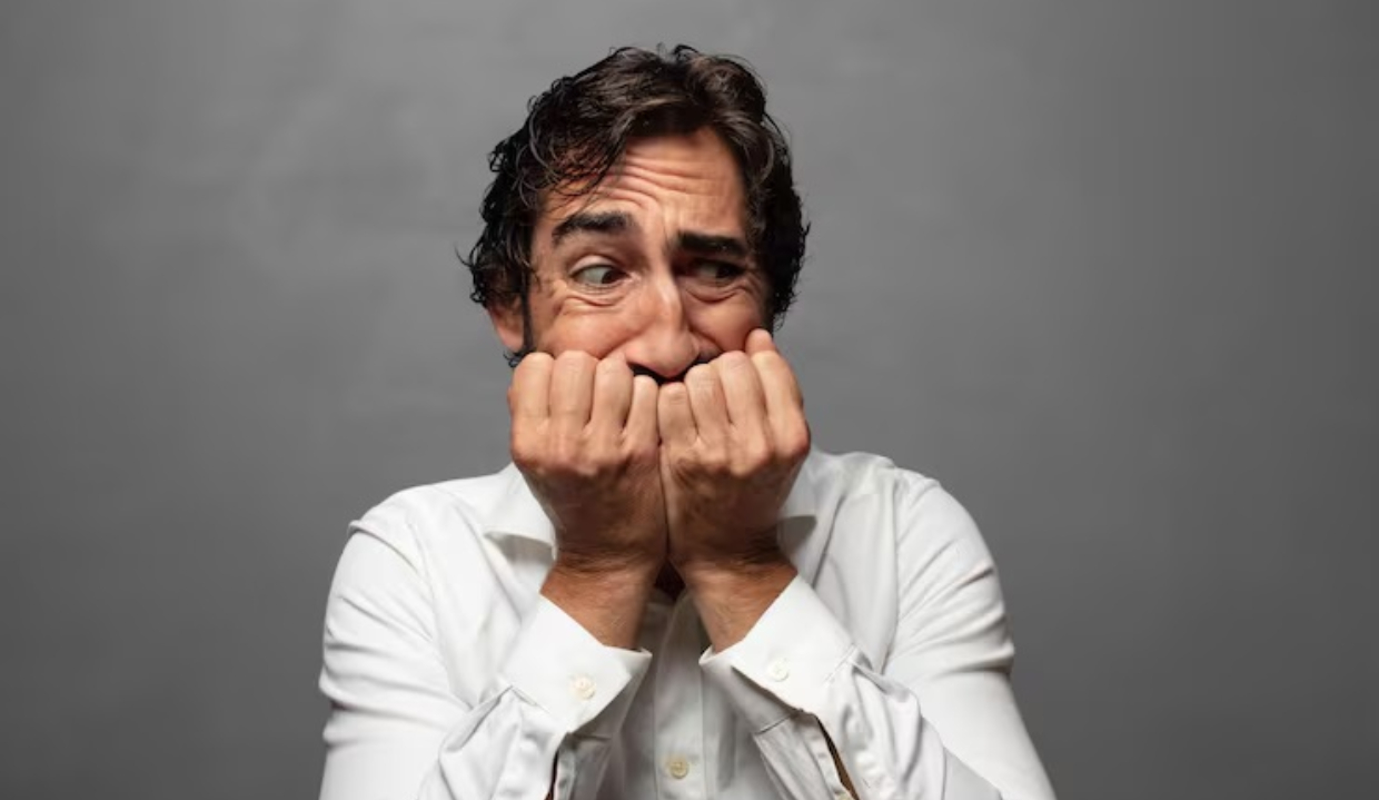 Homem de camisa branca com mãos no rosto e expressão de medo