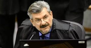 ministro Marco Buzzi sério, de óculos de grau, falando em microfone