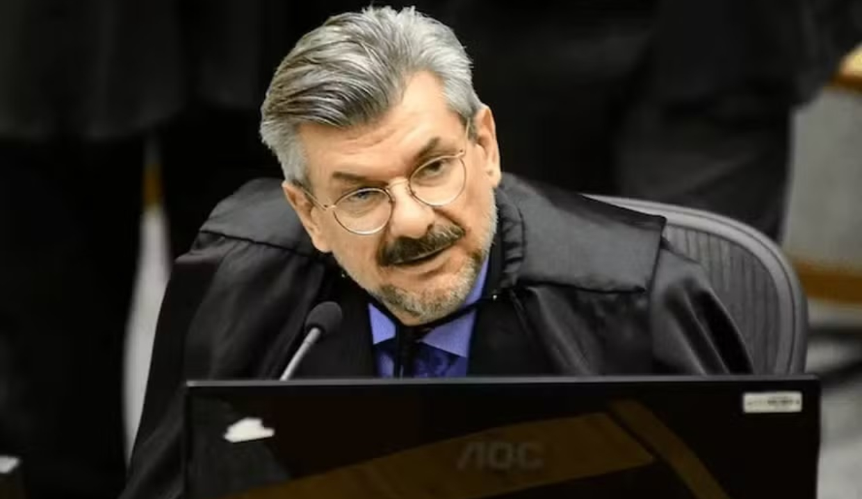 ministro Marco Buzzi sério, de óculos de grau, falando em microfone