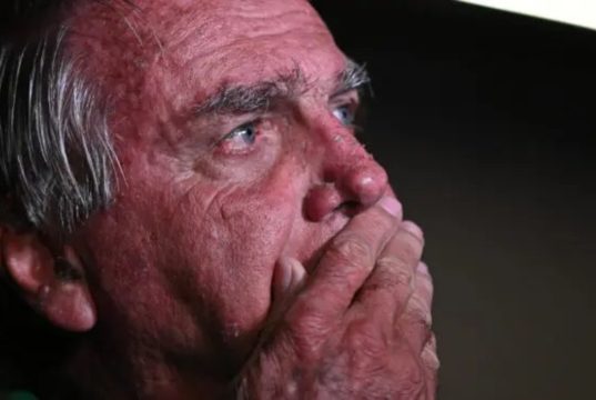 Jair Bolsonaro (PL) com expressão de preocupação e mão no rosto, em close