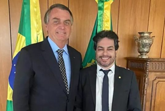 Jair Bolsonaro e Vinicius Gurgel (PL-AP) em pé, lado a lado, de roupa social, sorrindo para a câmera