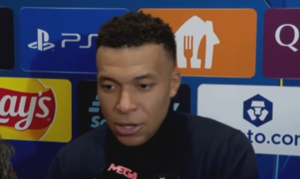 Kylian Mbappé falando, sério, sem olhar para a câmera, de roupa de frio escura