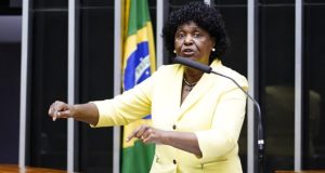deputada federal Benedita da Silva (PT) de roupa amarela, falando em microfone, na Câmara, gesticulando