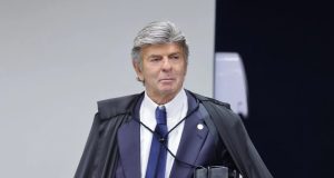 O ministro Luiz Fux sério, em pé, sem olhar para a câmera