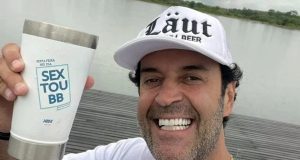 O influenciador Henrique Maderite de boné, segurando copo, sorrindo para a câmera