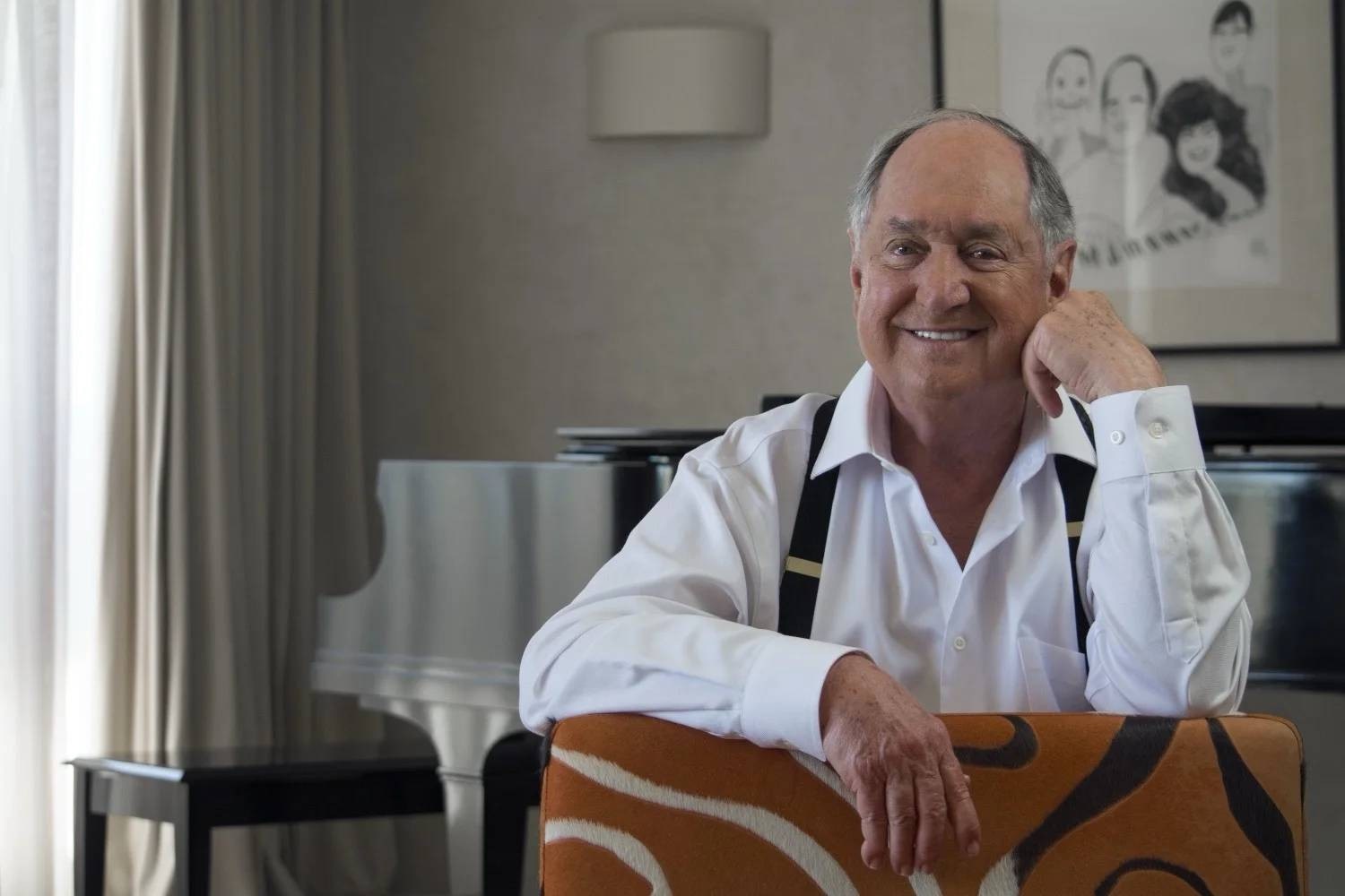 O cantor e compositor Neil Sedaka sorrindo para a câmera, de roupa social branca