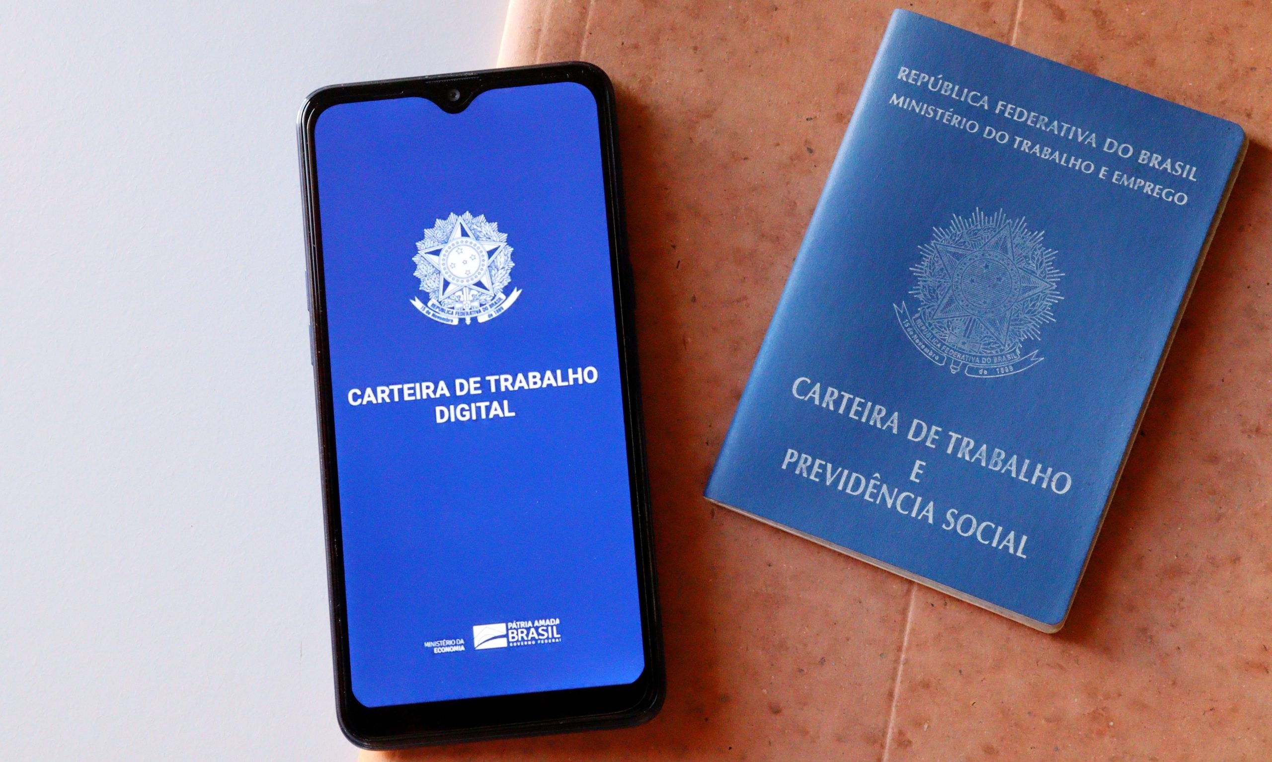 Celular com logo da Carteira de Trabalho e Carteira de Trabalho física