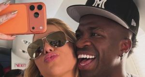 Virginia Fonseca e o jogador Vini Jr. sorrindo com as cabeças coladas em foto no espelho, ela de óculos escuros e ele de boné