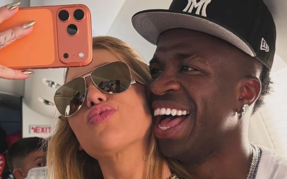 Virginia Fonseca e o jogador Vini Jr. sorrindo com as cabeças coladas em foto no espelho, ela de óculos escuros e ele de boné