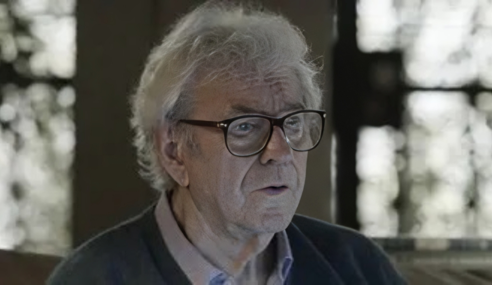 O ator Juca de Oliveira sério, de óculos de grau, em cena, sem olhar para a câmera