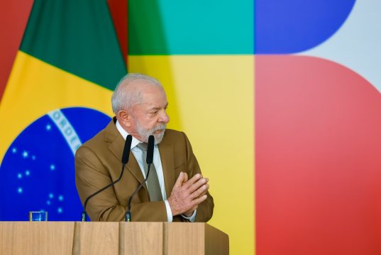 O presidente Luiz Inácio Lula da Silva (PT) de roupa social marrom, falando e gesticulando, olhando para o lado