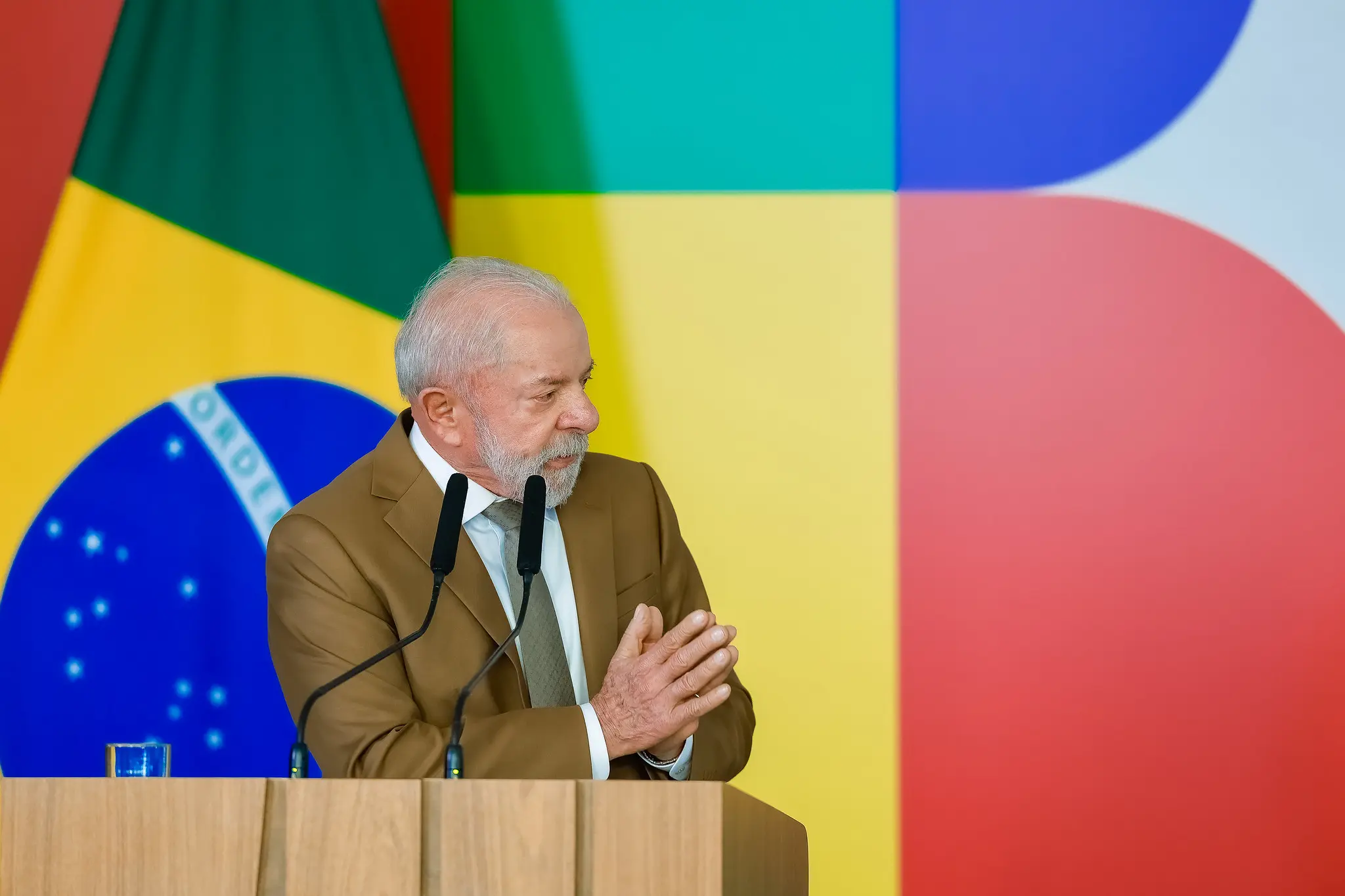 O presidente Luiz Inácio Lula da Silva (PT) de roupa social marrom, falando e gesticulando, olhando para o lado