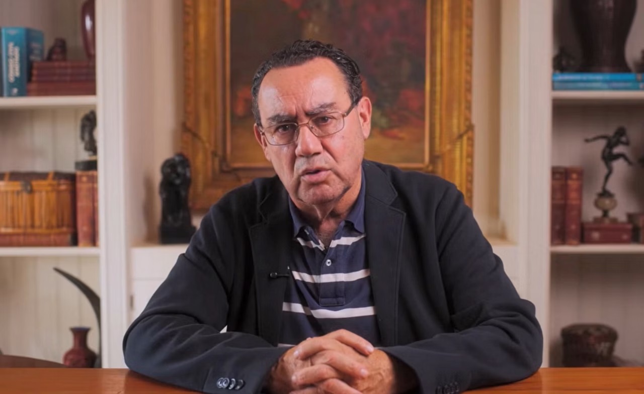 O escritor e psiquiatra Augusto Cury falando para a câmera, de óculos de grau, sentado