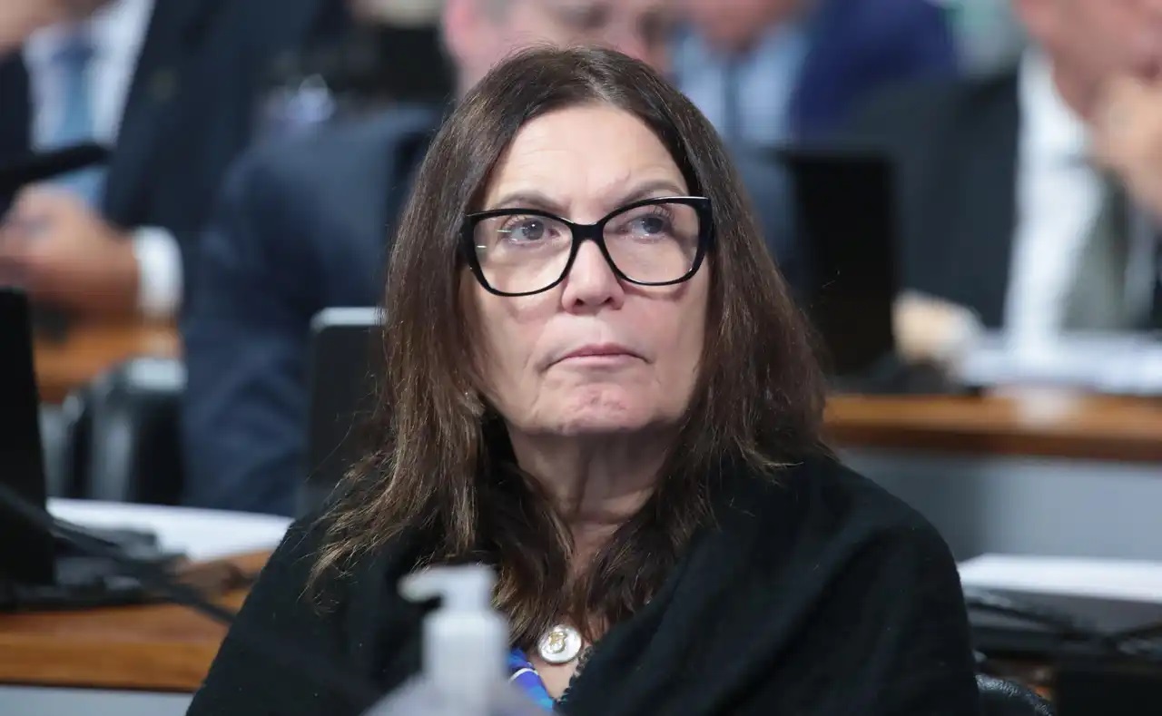 Bia Kicis séria, de óculos de grau, roupa preta e cabelo solto, olhando para o lado