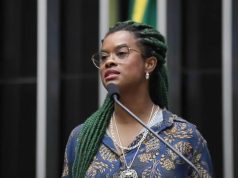 A deputada federal Carol Dartora (PT-PR) falando em microfone, séria