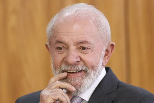 O presidente Luiz Inácio Lula da Silva (PT) com um dedo na boca, sorrindo, em close, sem olhar para a câmera