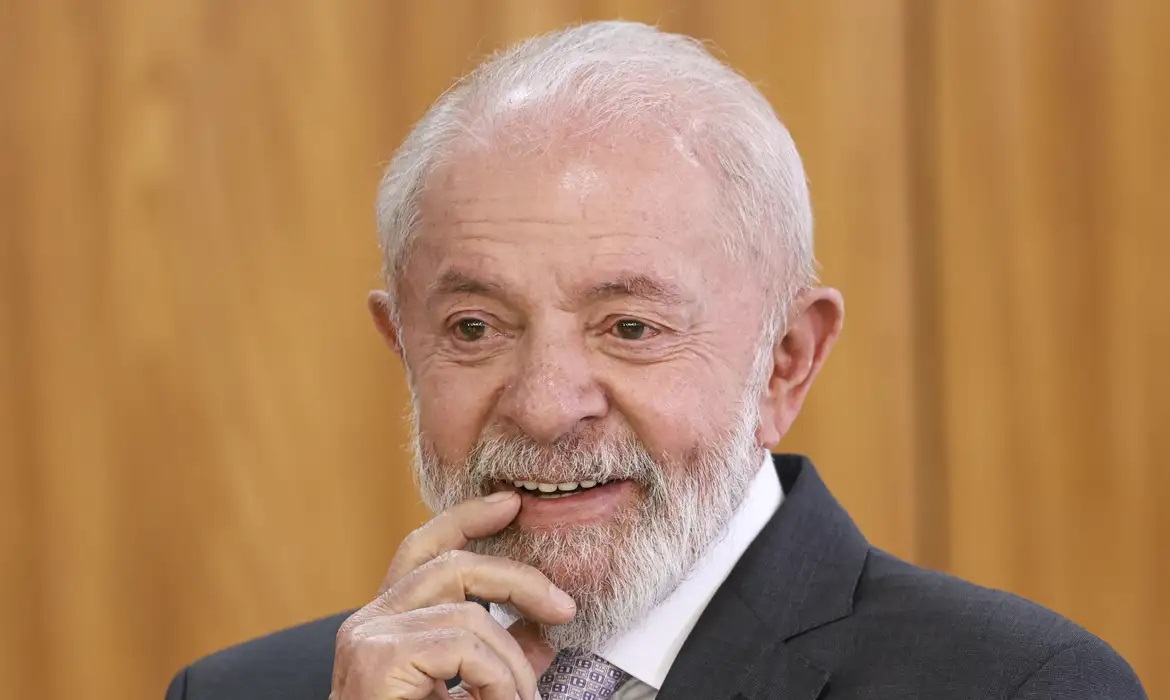O presidente Luiz Inácio Lula da Silva (PT) com um dedo na boca, sorrindo, em close, sem olhar para a câmera