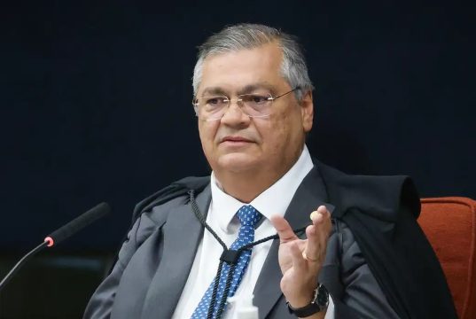 O ministro Flávio Dino, do Supremo Tribunal Federal (STF), sentado, falando e gesticulando, de óculos de grau
