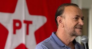 O presidente do PT, Edinho Silva, falando em microfone, no canto direito de foto, sério, sem olhar para a câmera