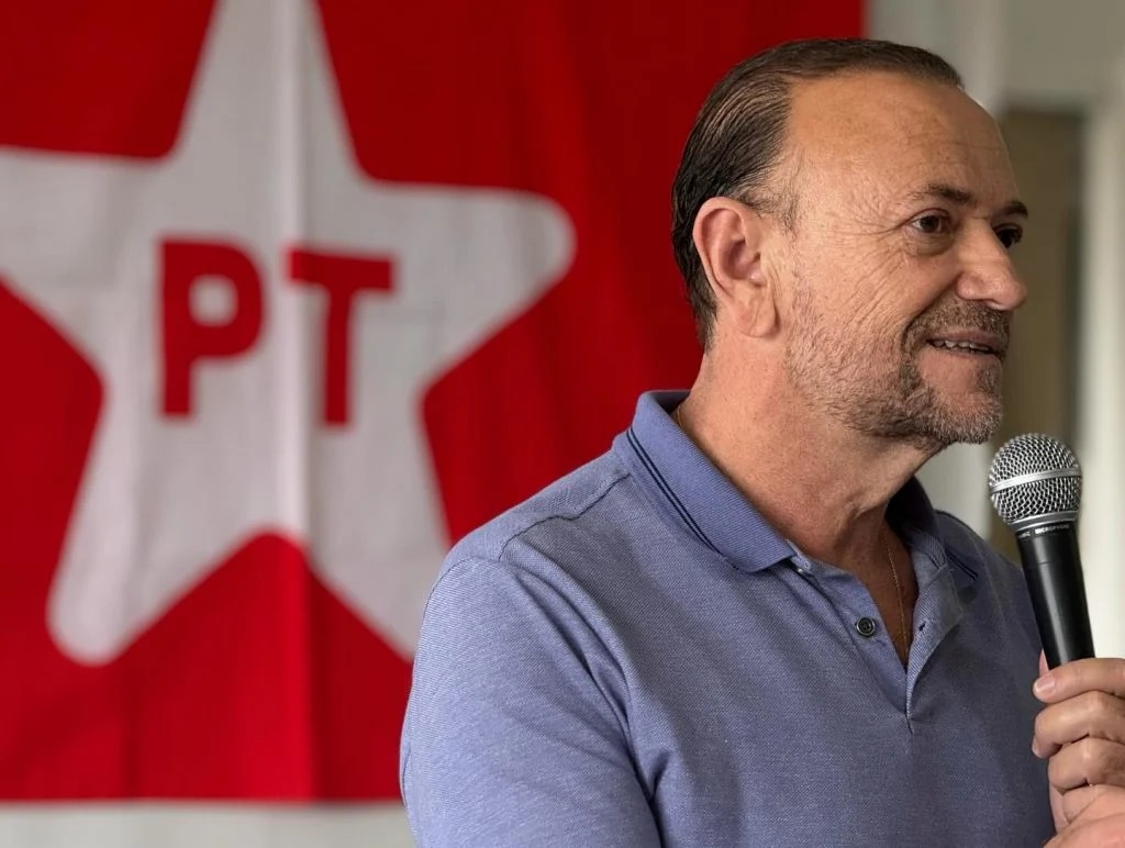 O presidente do PT, Edinho Silva, falando em microfone, no canto direito de foto, sério, sem olhar para a câmera