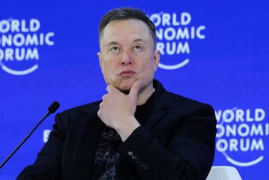 Elon Musk com expressão pensativa e a mão no queixo