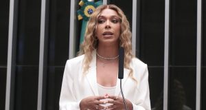 deputada federal Erika Hilton de roupa branca e cabelo solto, falando, em pé, séria