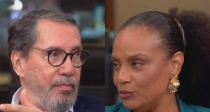 jornalistas Merval Pereira e Flávia Oliveira falando, sérios, se olhando