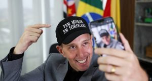 Rodrigo Manga (Republicanos) de boné, sorrindo e olhando para celular