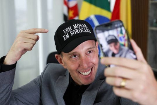 Rodrigo Manga (Republicanos) de boné, sorrindo e olhando para celular