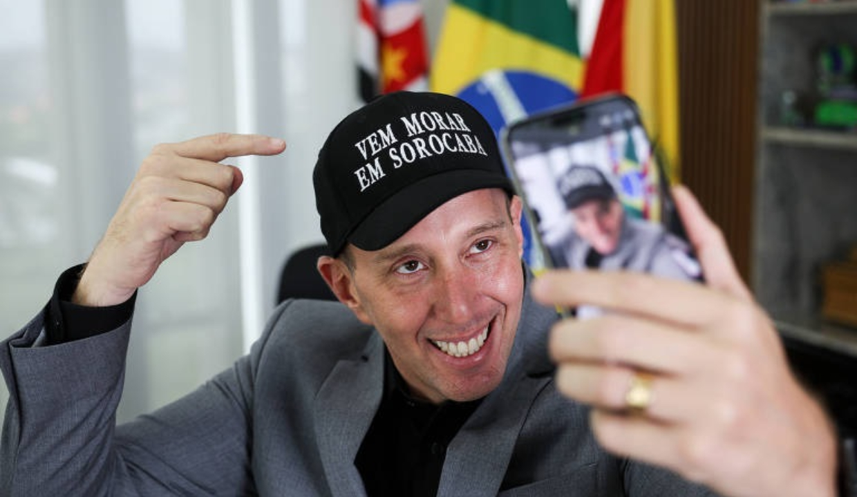 Rodrigo Manga (Republicanos) de boné, sorrindo e olhando para celular