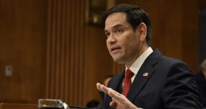 O secretário de Estado dos EUA, Marco Rubio, em pé, falando e gesticulando, sério, sem olhar para a câmera