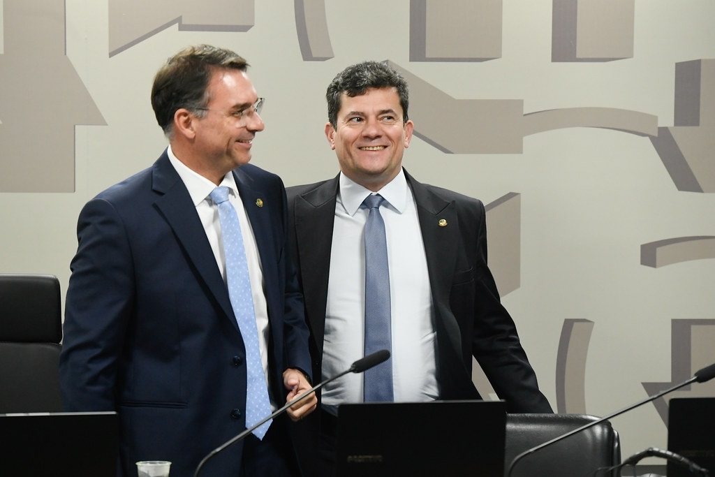 Os senadores Flavio Bolsonaro (PL) e Sergio Moro (União) em pé, lado a lado, sorrindo
