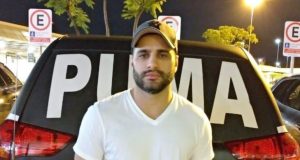 Luiz Phillipi Mourão, conhecido como “Sicário”, posando para foto de camiseta branca e boné, sério, olhando para a câmera