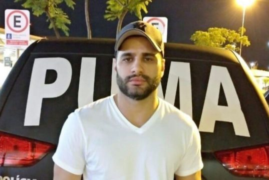 Luiz Phillipi Mourão, conhecido como “Sicário”, posando para foto de camiseta branca e boné, sério, olhando para a câmera