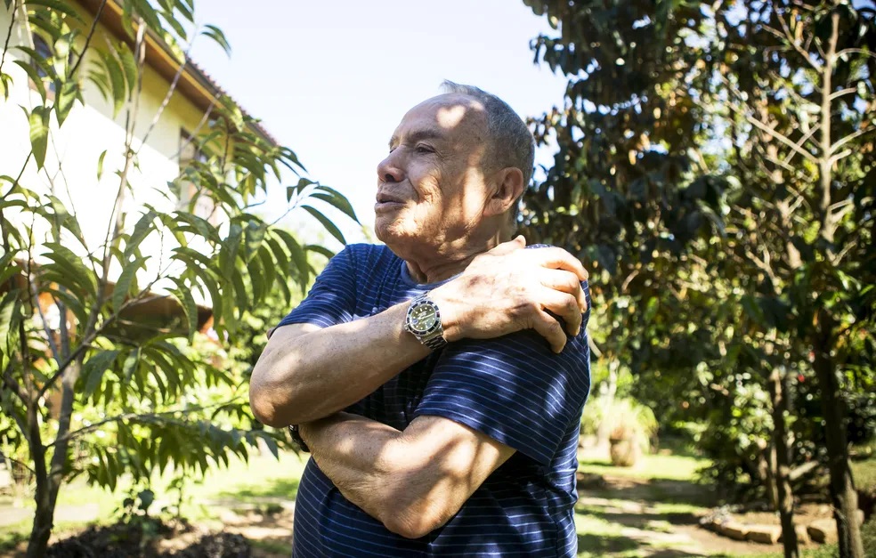 Stênio Garcia de braços cruzados, falando, em pé, de perfil