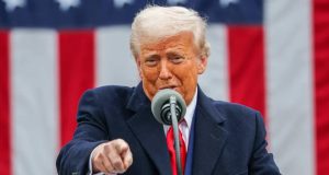 O presidente americano Donald Trump falando em microfone e apontando pra frente