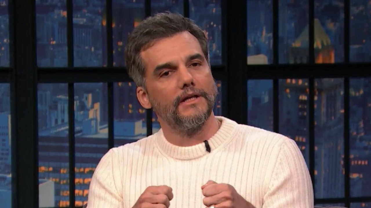 Wagner Moura falando e gesticulando, sério, de roupa de frio clara