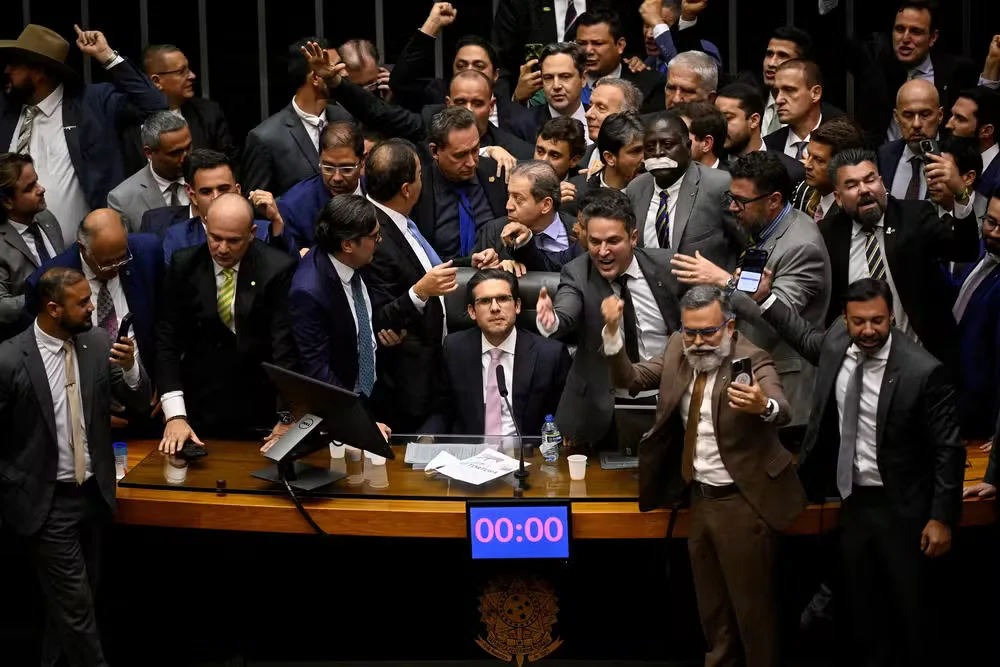 O presidente da câmara Hugo Motta, sentado na mesa da presidência, logo após retomar controle do plenário em motim na Câmara, liderado por bolsonaristas.