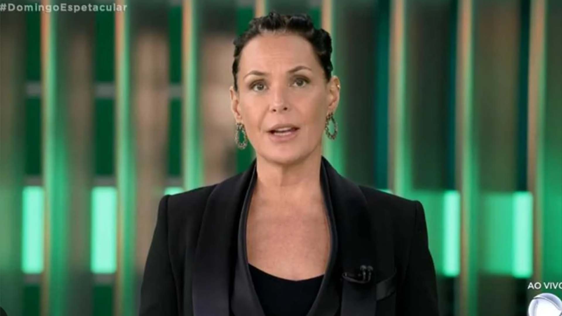 Carolina Ferraz de roupa social preta e cabelo preso, falando para a câmera