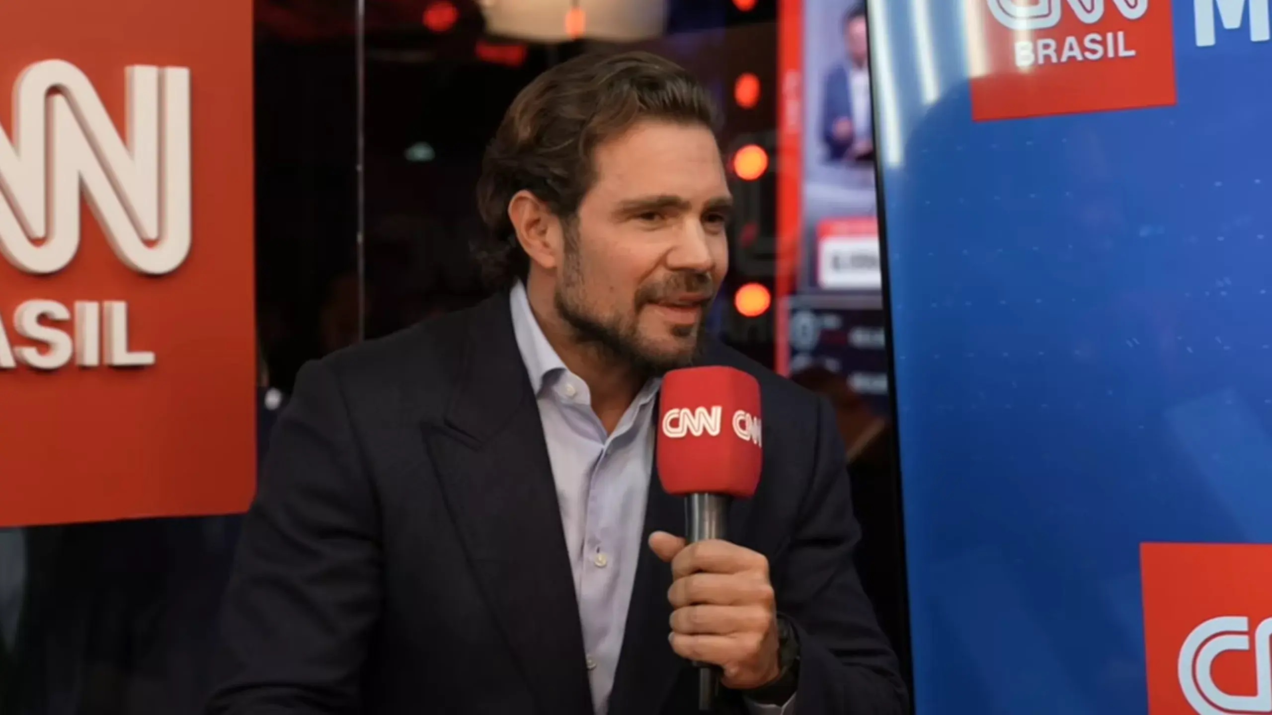 empresário Daniel Vorcaro falando em microfone da CNN Brasil, sem olhar para a câmera, sentado